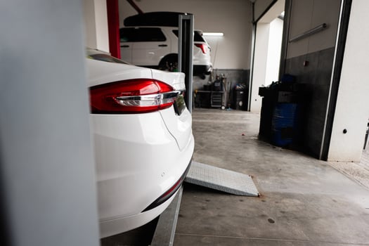 White car on lift in auto repair garage with vehicle in background photo