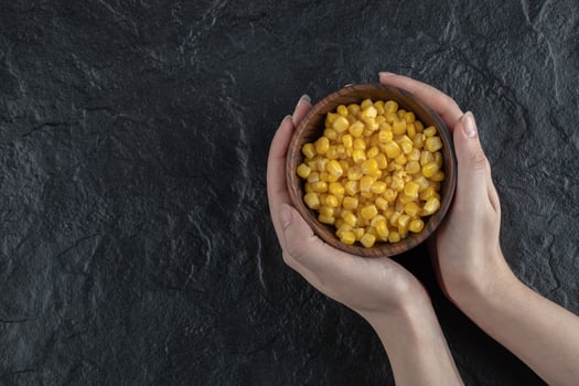 Female holding Canned sweet corn in bowl over black background photo