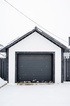 A black and white garage door stands wide open in a heavy layer of snow, showcasing the contrast between the dark door and the bright, white winter landscape surrounding it photo