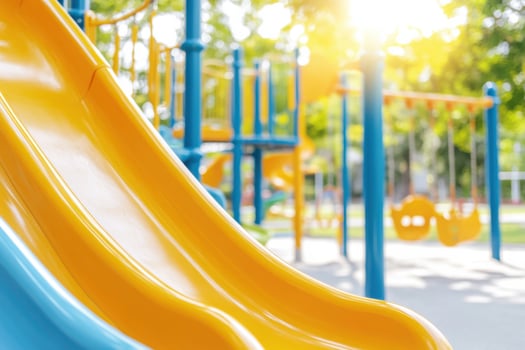 Whimsical playground for children featuring yellow slides and swings surrounded by green trees under bright sunlight photo