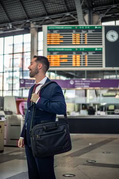 vertical smiling businessman with briefcase waiting by train station information screens photo