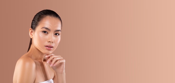 Asian woman applies a skincare product while relaxing and pampering herself in a minimalistic setting. The soft background enhances her natural beauty and care routine. photo