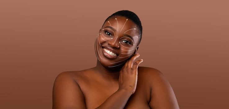 African American woman engages in her skin care routine, smiling as she pampers herself. Her skin is adorned with a unique design, showcasing her beauty in a serene, isolated environment. photo