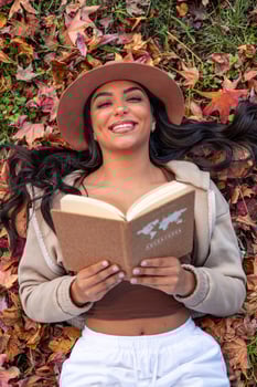 Young latin woman reading a book about adventures lying on autumn leaves photo