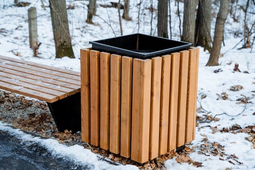 A charming wooden trash can is positioned next to a beautifully crafted wooden bench, both elegantly blanketed in pristine white snow, collectively creating a truly picturesque winter scene photo