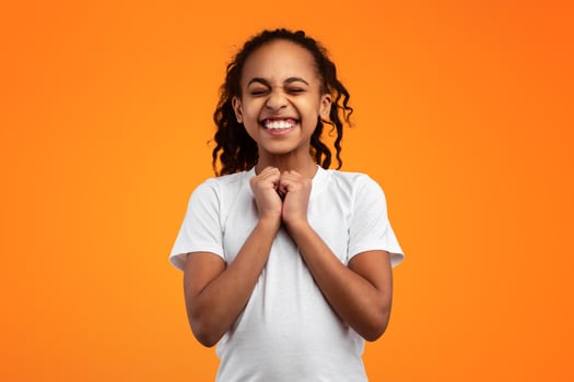 Excited black girl anticipating something wonderful, making wish, begging or praying over yellow orange studio background. Hopeful African American teen wishing for good luck, waiting for miracle photo