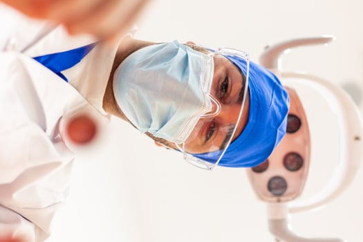 POV Dentist wearing surgical mask and protective glasses examining patient's teeth photo