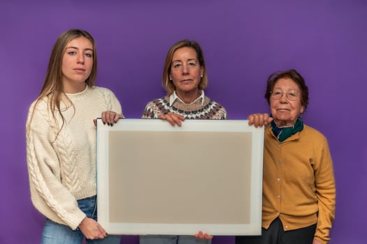 Three women of different ages holding a blank canvas against a purple background photo
