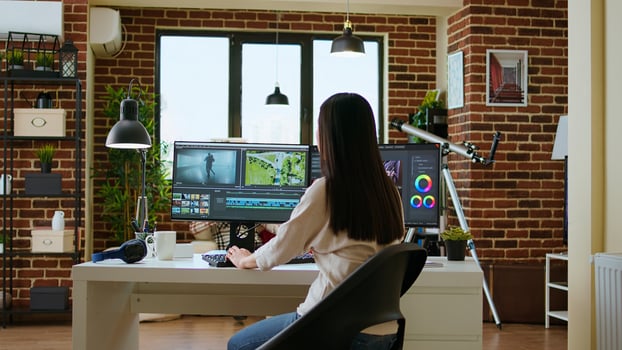 Asian woman edits videos in a creative software at her home office. Filmmaker using dual monitors and color wheel to work on footage in post production, highlighting remote work lifestyle. Camera A. photo