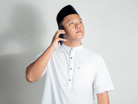 Muslim Asian man using white shirt and black cap talking on mobile phone device photo