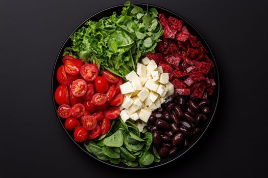 Healthy Mediterranean salad with feta cheese, olives, tomatoes, and salami in a black bowl photo