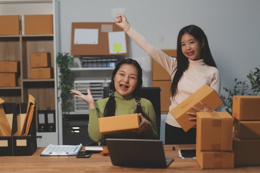 Two women in an office with boxes and a laptop photo
