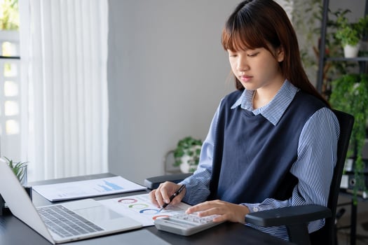 Asian businesswoman doing paper work with pen laptop calculator at desk photo