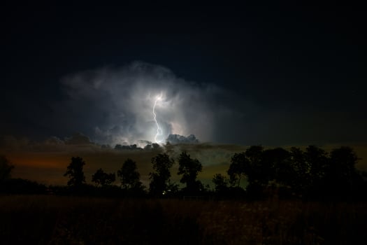 A lightning bolt is seen in the sky over a field photo