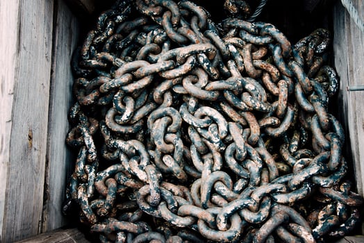 Large rusty big metal chain from ship anchor lying in wooden box, rebar texture photo