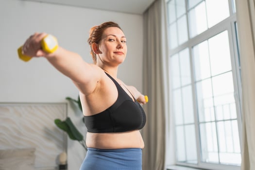 Fitness workout training. Woman picking up dumbbells. Plus size female doing sports exercise at home indoor. Girl in sportswear have workout weight training for weight loss. Sport and fitness photo