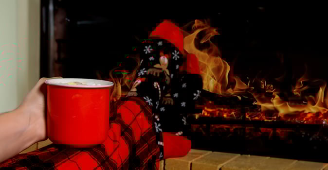 close-up women's legs in vibrant Christmas socks and plaid pants rest comfortably near a fireplace, holding a warm drink photo