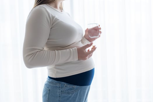 Pregnant woman holding a glass of water, taking vitamins and supplements during pregnancy with copy space. Pregnancy, health, pharmaceuticals. Close up photo
