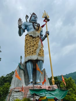 A remarkable large statue of a deity triumphantly holding a trident stands majestically, surrounded by the sky and clouds, surrounded by lush greenery, showcasing stunning art photo