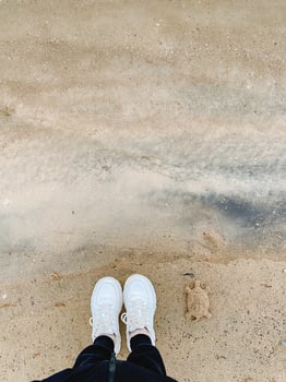 There is an individual who is wearing white sneakers standing on a sandy beach with the ocean nearby, enjoying the warm weather and the beautiful sandy landscape around them photo