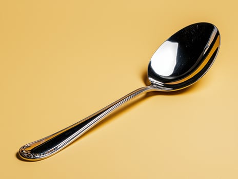 Shiny silver spoon on yellow background photo