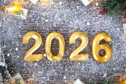 Happy New Year golden numbers 2026 cozy festive grey wooden background with Christmas tree, snow, lights of garlands. Greetings, postcard. Calendar, cover photo