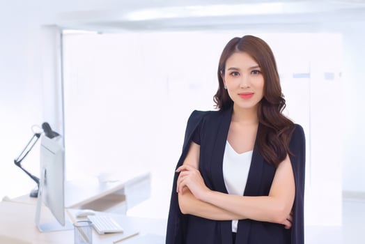 Young beautiful asian professional businesswoman standing with crossed arms in office workspace while looking at camera photo