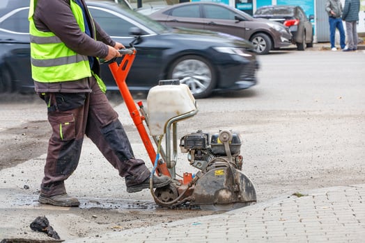 A road worker cuts with a petrol cutter and a diamond wheel the old asphalt on the carriageway of a city street. photo