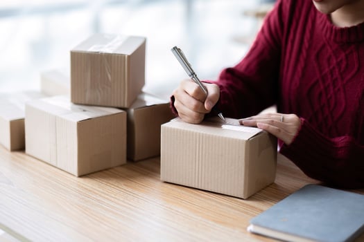 A small SME business owner receives product orders and writes shipping information on cardboard boxes in the home office to prepare for delivery. photo