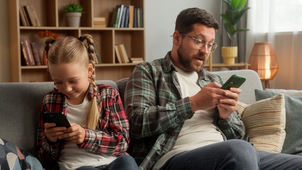 Caucasian Internet addicted male dad guy man kid daughter family using mobile phone smartphone dependency at home sofa little girl child parent father playing digital game online family technology app photo