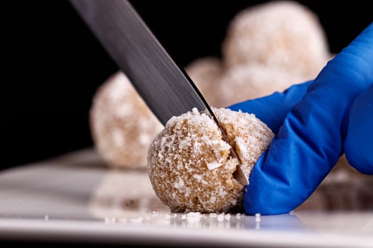Beautiful sweets with coconut are cut with a knife on a white plate on a black background close up photo