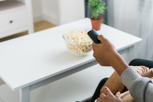 Hand holds a remote control while a bowl of popcorn sits on a white table in a modern living room. Relaxing and cozy atmosphere, perfect for watching movies or streaming content at home photo