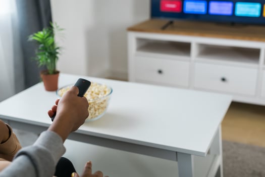 Hand holds a remote control while a bowl of popcorn sits on a white table in a modern living room. Relaxing and cozy atmosphere, perfect for watching movies or streaming content at home photo