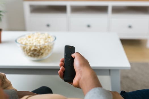 Hand holds a remote control while a bowl of popcorn sits on a white table in a modern living room. Relaxing and cozy atmosphere, perfect for watching movies or streaming content at home photo