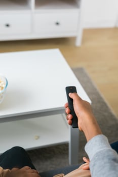 Hand holds a remote control while a bowl of popcorn sits on a white table in a modern living room. Relaxing and cozy atmosphere, perfect for watching movies or streaming content at home photo