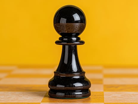 Black chess pawn on a yellow and beige chessboard photo
