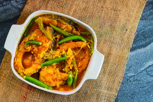 Close-up of fish curry with green chili in a white ceramic bowl on a black background photo