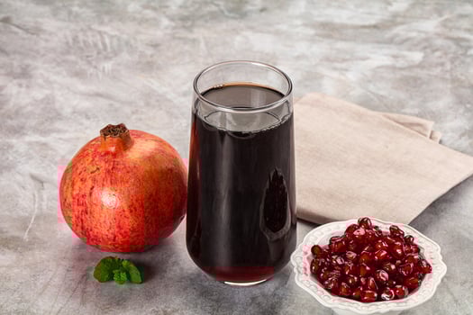 A glass of liquid next to a bowl of pomegranate photo