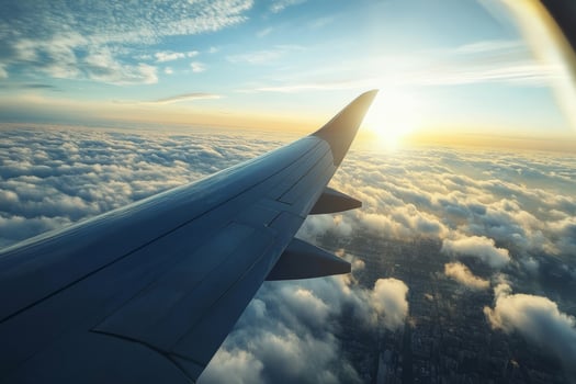 Experience the breathtaking beauty of a serene morning flight, with sunlight glistening on the wing as you glide over a vibrant city, surrounded by fluffy clouds in a clear blue sky photo