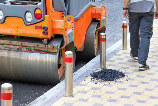 The metal wheels of the agile road roller compact the fresh asphalt on the stretch of road along the sidewalk. photo