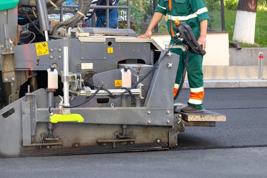 A fragment of the work of an industrial asphalt paver, an engineer stands on the footboard and controls the process. photo