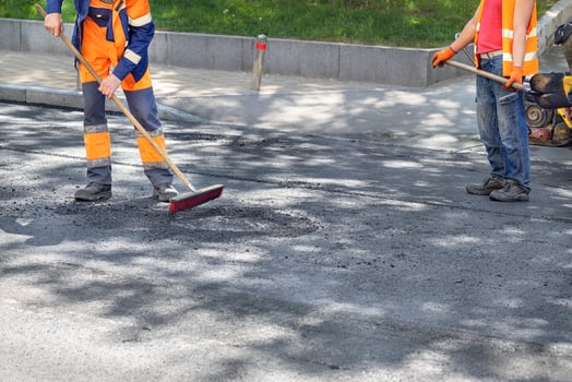 A road maintenance workers cleans up the new asphalt pavement on the carriageway with a brush and shovel. photo
