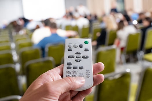 A hand is skillfully holding a remote control while in a conference setting with an engaged audience present photo