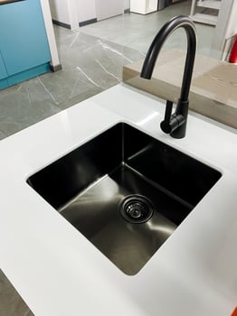In a modern kitchen, there is a striking black sink paired with a sleek black faucet that sits elegantly atop a pristine white countertop. This design enhances the overall aesthetic photo