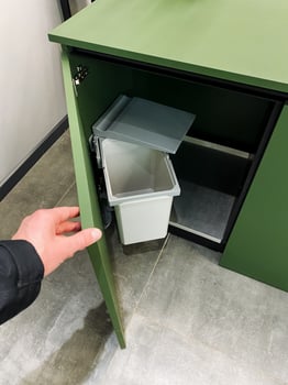 A person is opening a green cabinet with a white trash can inside photo
