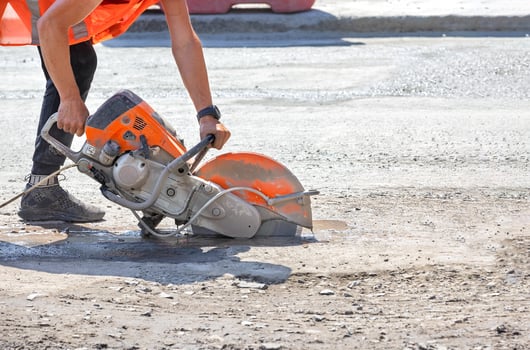 A petrol disc cutter in the hands of a worker cuts the asphalt concrete road surface on a sunny summer day. photo