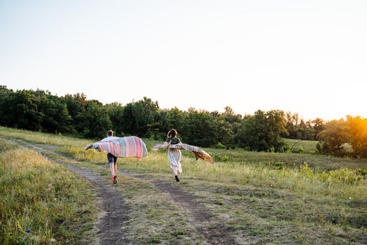 Joyful and carefree friends running through a serene meadow at sunset, enjoying colorful blankets and vibrant nature together with happiness photo