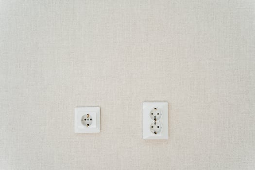 Two white wall sockets shaped like rectangles hang on the white wall photo