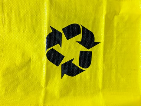 The item in question is a vibrant yellow bag that features a bold black recycling symbol prominently displayed upon its surface, indicating its environmental significance photo