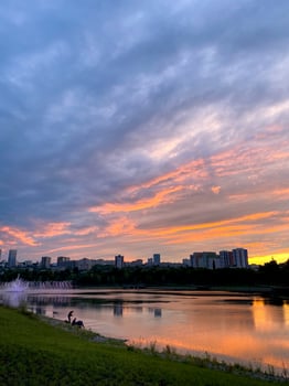 A stunning sunset gracefully casts its colors over a serene lake, while a vibrant city skyline stands majestically in the background, creating a picturesque blend of nature and urban life photo